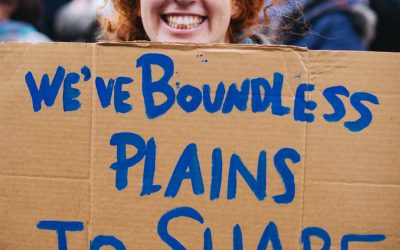 Smiling woman holding protest sign that reads "We've boundless plains to share"